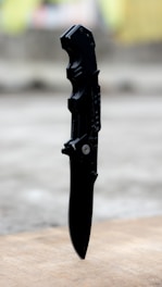 Close-up of a matte black tactical knife resting on a dark textured surface, highlighting its sharp edge and sturdy grip.