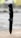 A black folding knife with a tactical tanto blade is positioned vertically on a wooden surface. The knife features a textured handle and appears sharp and sturdy. The background is blurred, suggesting an outdoor setting.