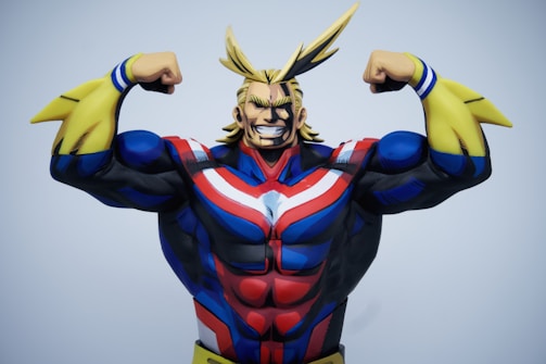 A muscular animated character with exaggerated features stands confidently, wearing a colorful costume with blue, red, and white stripes alongside yellow gauntlets. The character's blonde hair is styled in pointed shapes, and they are posed flexing both arms to showcase strength and power.