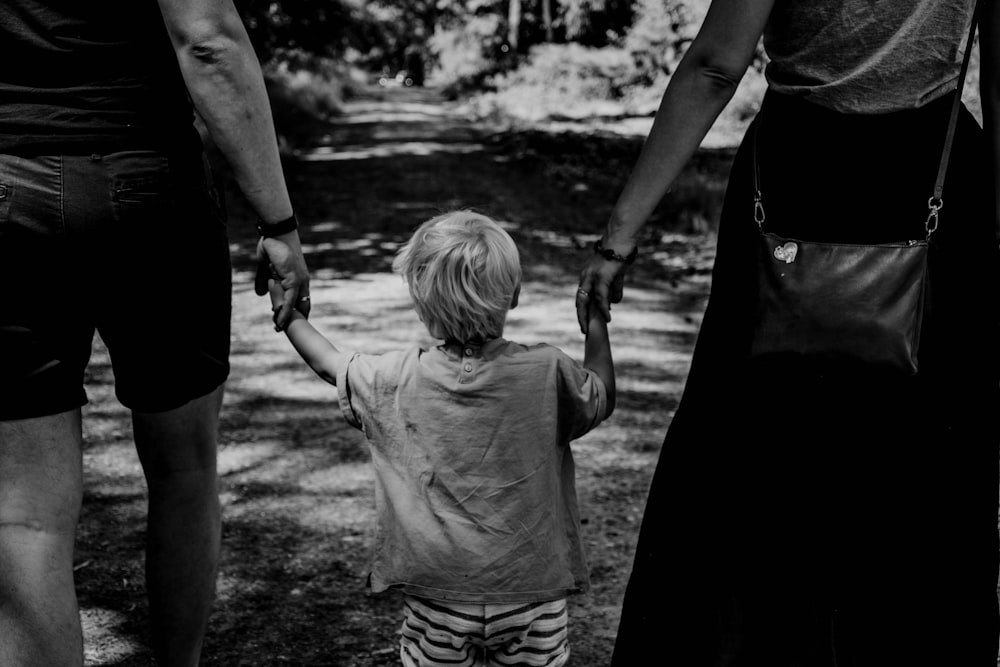 Foto in scala di grigi di donna in abito nero che tiene bambino in camicia nera