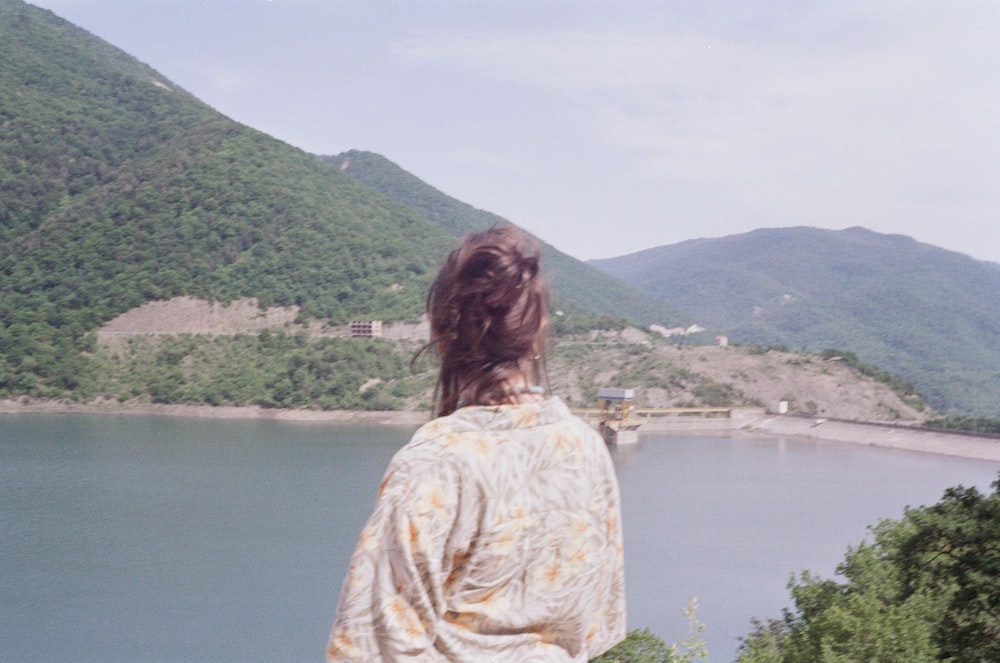 woman in white and yellow floral shirt standing near lake during daytime
