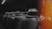 Various beverage cans and bottles are arranged in rows. The image has a dark ambiance with a burst of orange light on the right side, creating a moody and mysterious atmosphere.