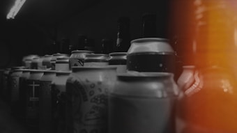 Various beverage cans and bottles are arranged in rows. The image has a dark ambiance with a burst of orange light on the right side, creating a moody and mysterious atmosphere.