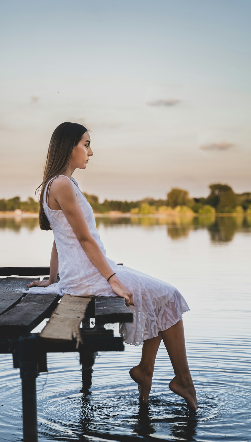 woman in white tank dress sitting on wooden dock during daytime