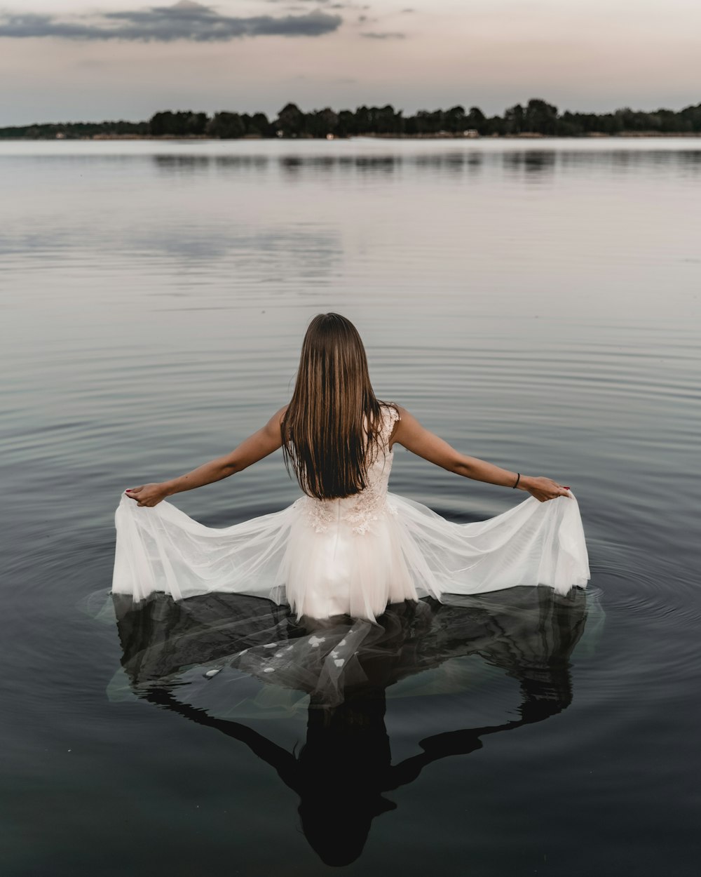 donna in vestito bianco che si siede sulla roccia in mezzo all'acqua