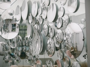 Numerous circular mirrors of varying sizes are mounted on a wall, creating an artistic and visually striking pattern of reflections. The mirrors reflect parts of the surrounding room, introducing a fragmented and abstract image of the environment, including furniture and decor.