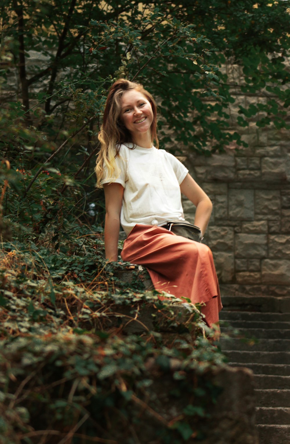 woman in white tank top and red skirt sitting on brown concrete wall during daytime