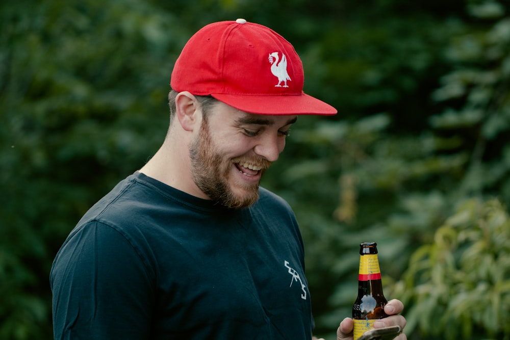 man in blue crew neck shirt and red cap holding bottle of beer