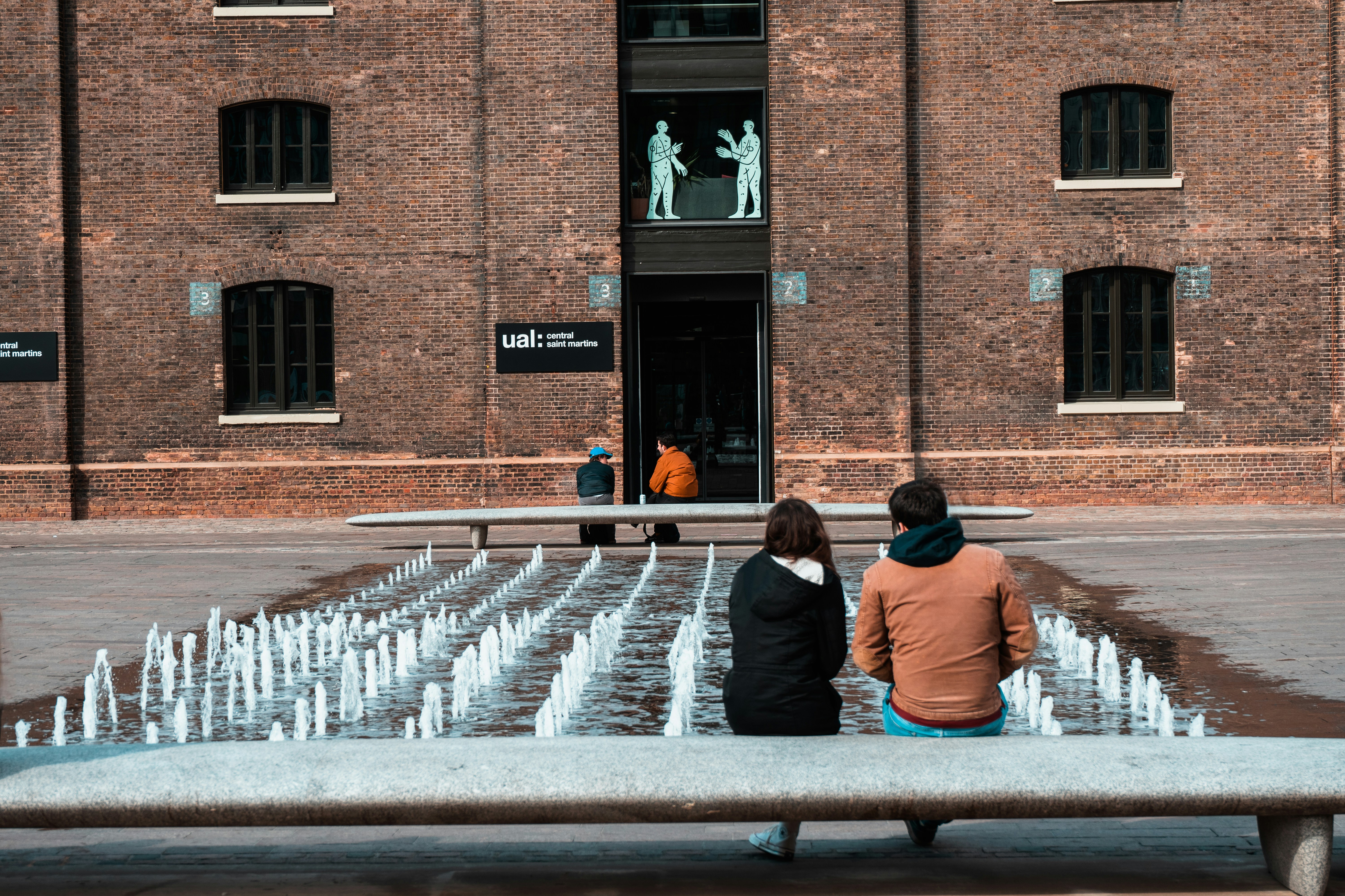 3 women sitting on bench in front of brown building during daytime