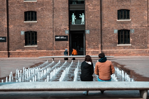 3 women sitting on bench in front of brown building during daytime