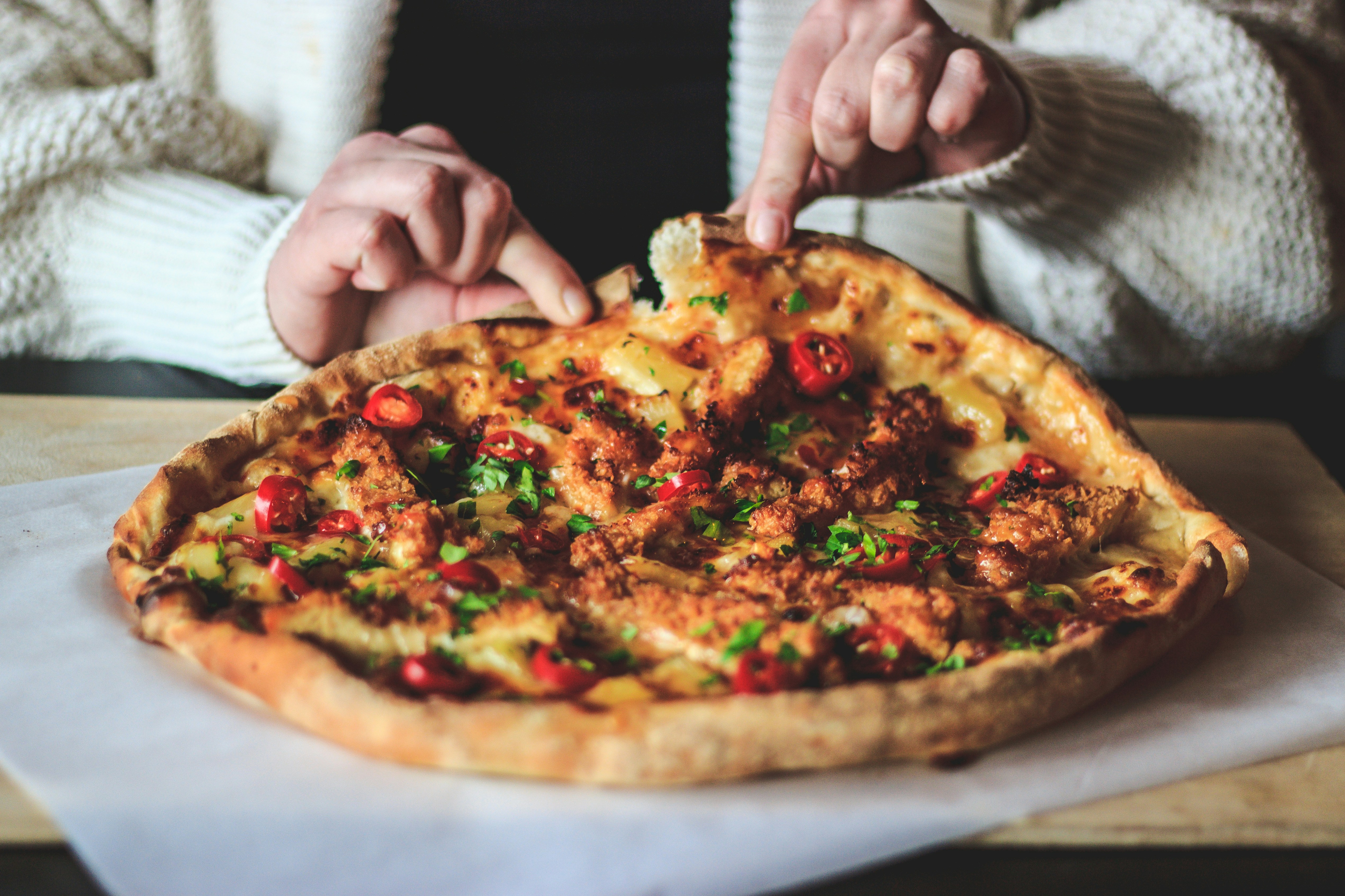 person holding pizza with cheese and green leaves