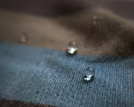 Close-up of a drop of cleanser on soft beige fabric with light gold accents.