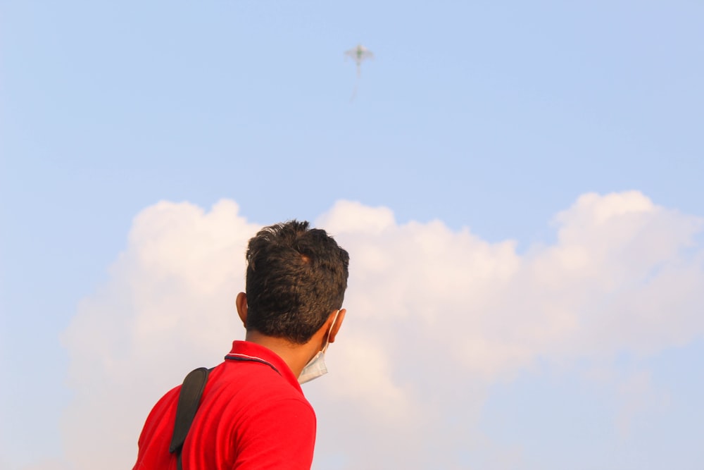 man in red hoodie looking at airplane in the sky during daytime