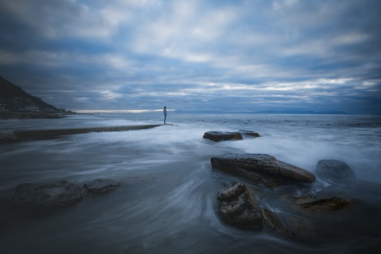 person standing on rock formation on sea under blue sky during daytime
