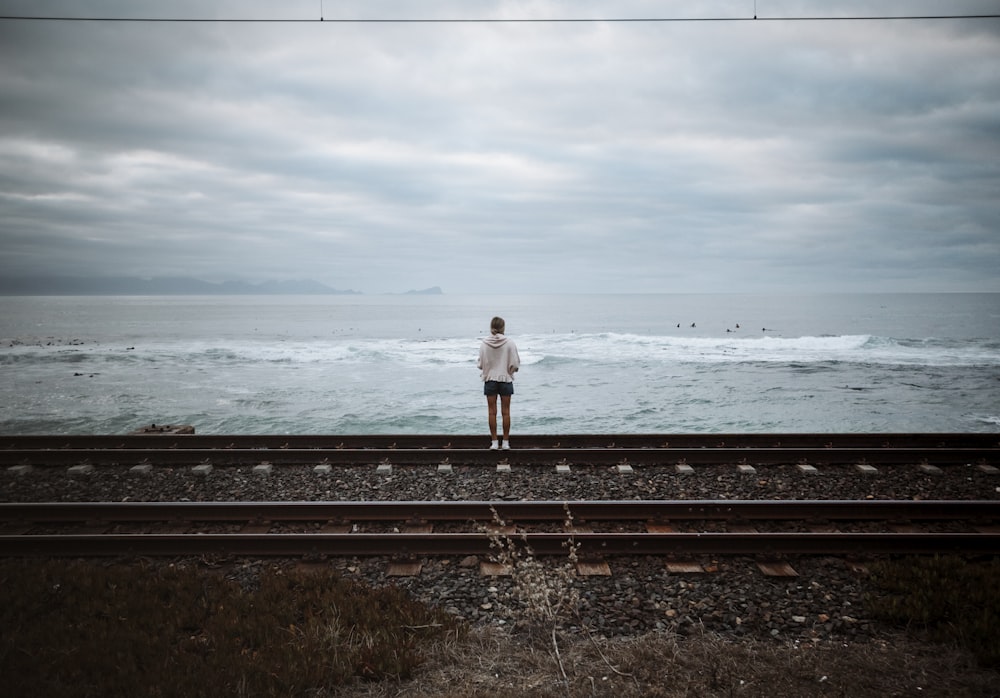 woman in white long sleeve shirt and black pants standing on black metal rail near sea