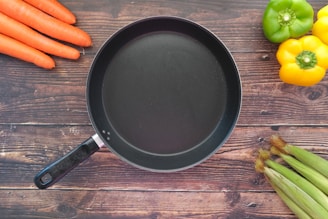 A sleek stick & fin frying pan resting on a rustic wooden countertop with fresh vegetables around.
