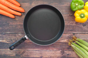 A black non-stick frying pan with fresh vegetables sizzling inside.