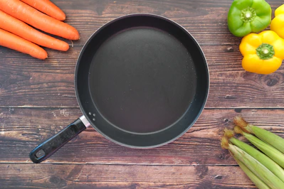 A sleek nonstick frypan with a wooden handle resting on a stovetop with fresh vegetables nearby