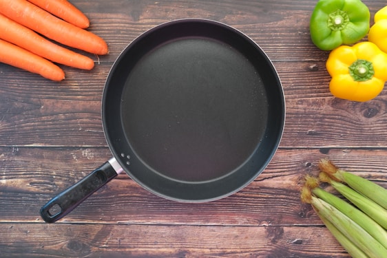 A sleek stick & fin frying pan resting on a rustic wooden countertop with fresh vegetables around.