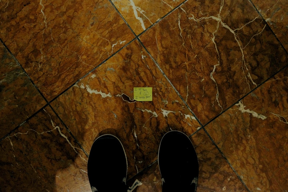 pessoa em calças pretas e sapatos pretos em pé sobre azulejos de piso marrom