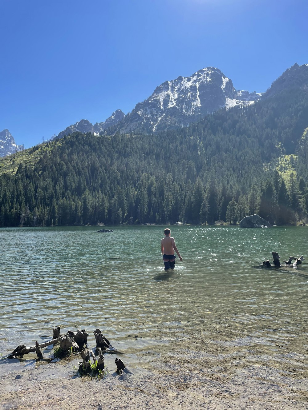 mujer con camisa roja y pantalones negros de pie sobre el agua cerca de árboles verdes y montaña durante