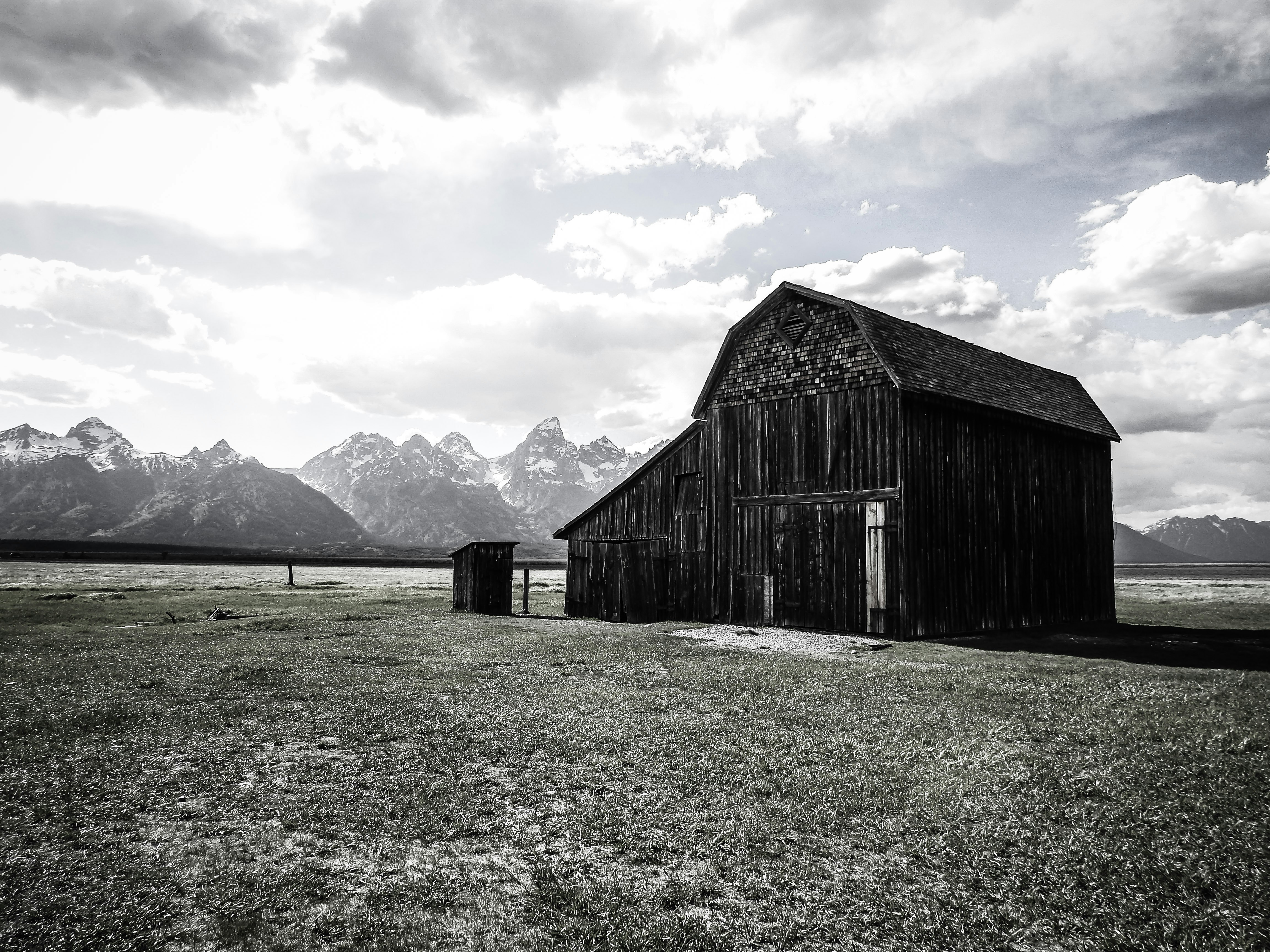 brown wooden barn on green grass field near mountains under white clouds during daytime