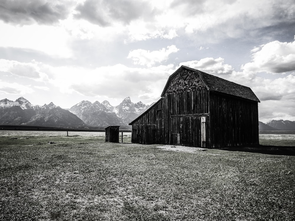 brown wooden barn on green grass field near mountains under white clouds during daytime