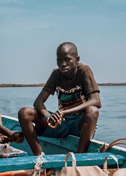 boy in brown crew neck t-shirt sitting on blue and white boat during daytime