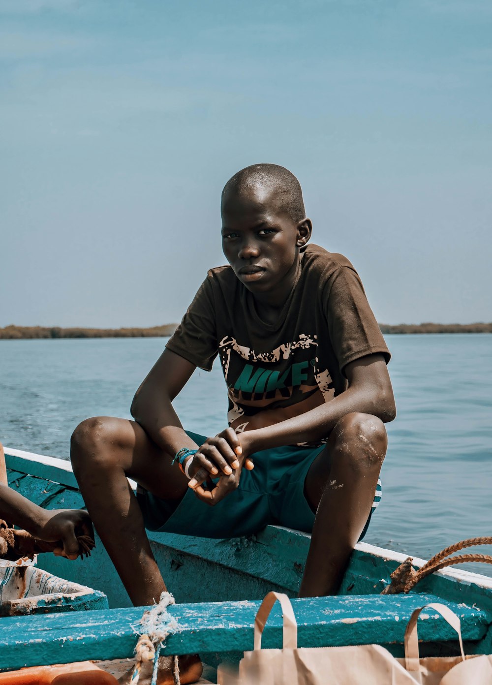 boy in brown crew neck t-shirt sitting on blue and white boat during daytime