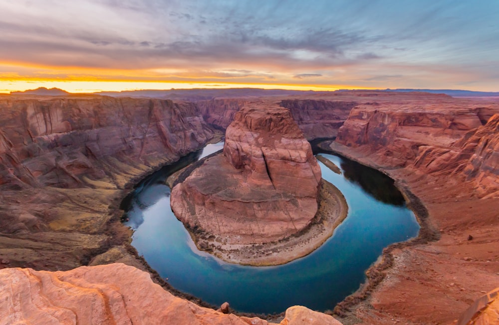 brown rock formation in the middle of lake during sunset