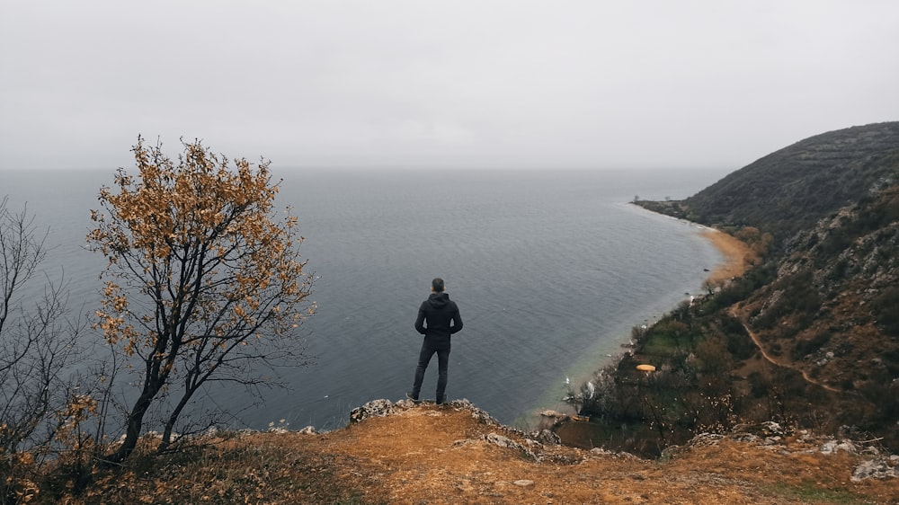 man in black jacket standing on rock near body of water during daytime