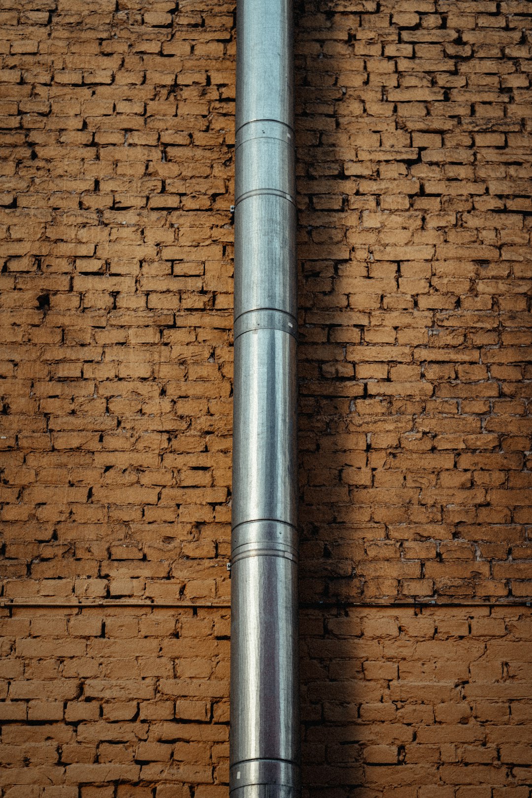 gray metal pipe on brown brick wall