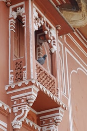 A detailed and ornately decorated balcony with traditional architectural elements, featuring intricate carvings. A pigeon is perched on the ledge.