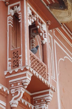 A detailed and ornately decorated balcony with traditional architectural elements, featuring intricate carvings. A pigeon is perched on the ledge.