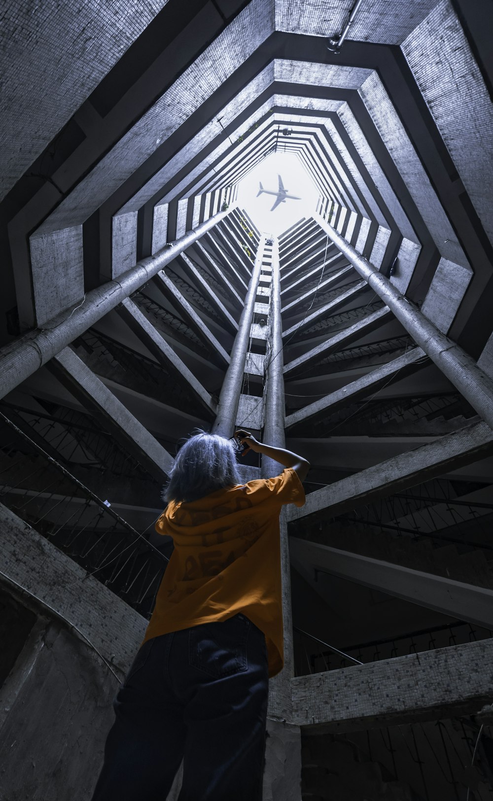 man in orange hoodie standing on gray concrete stairs