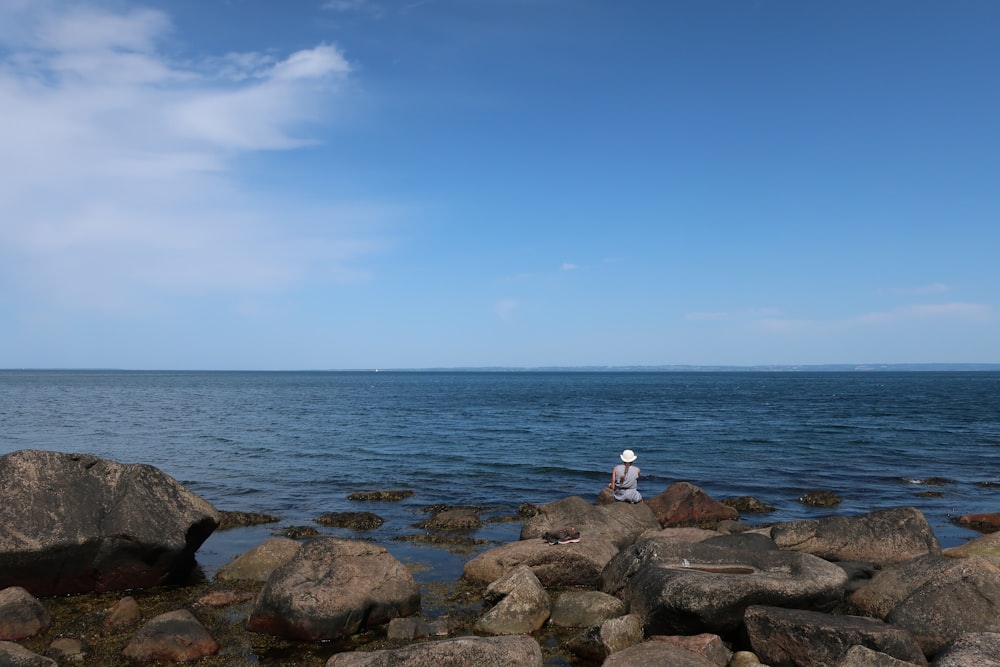 person in white shirt sitting on rock near sea during daytime