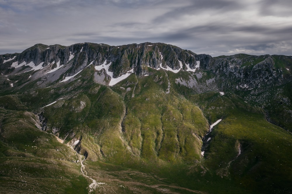 montagnes vertes et grises sous un ciel nuageux blanc pendant la journée