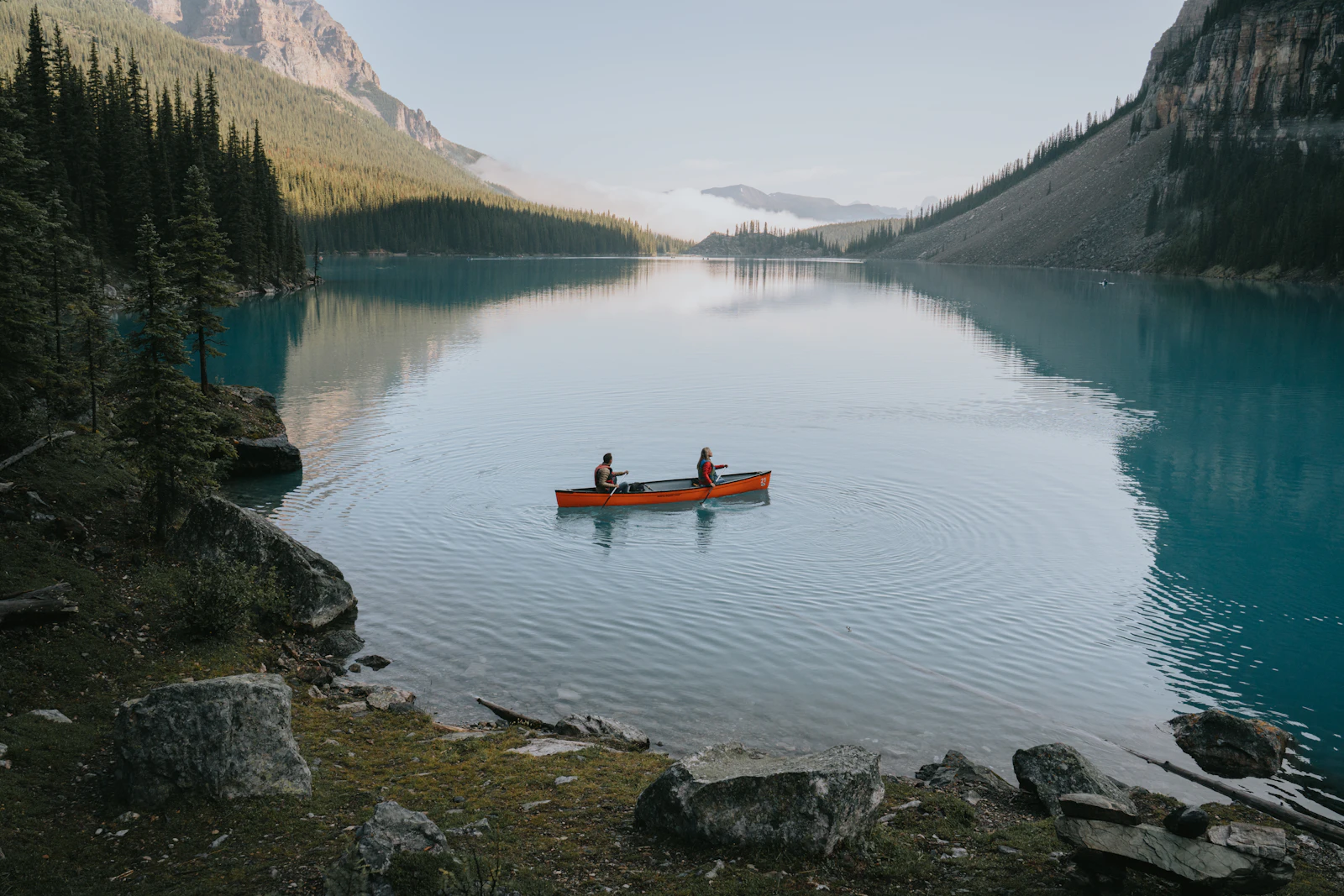 Canoë rouge sur un lac paisible entouré de forêts et de montagnes dans les Rocheuses canadiennes
