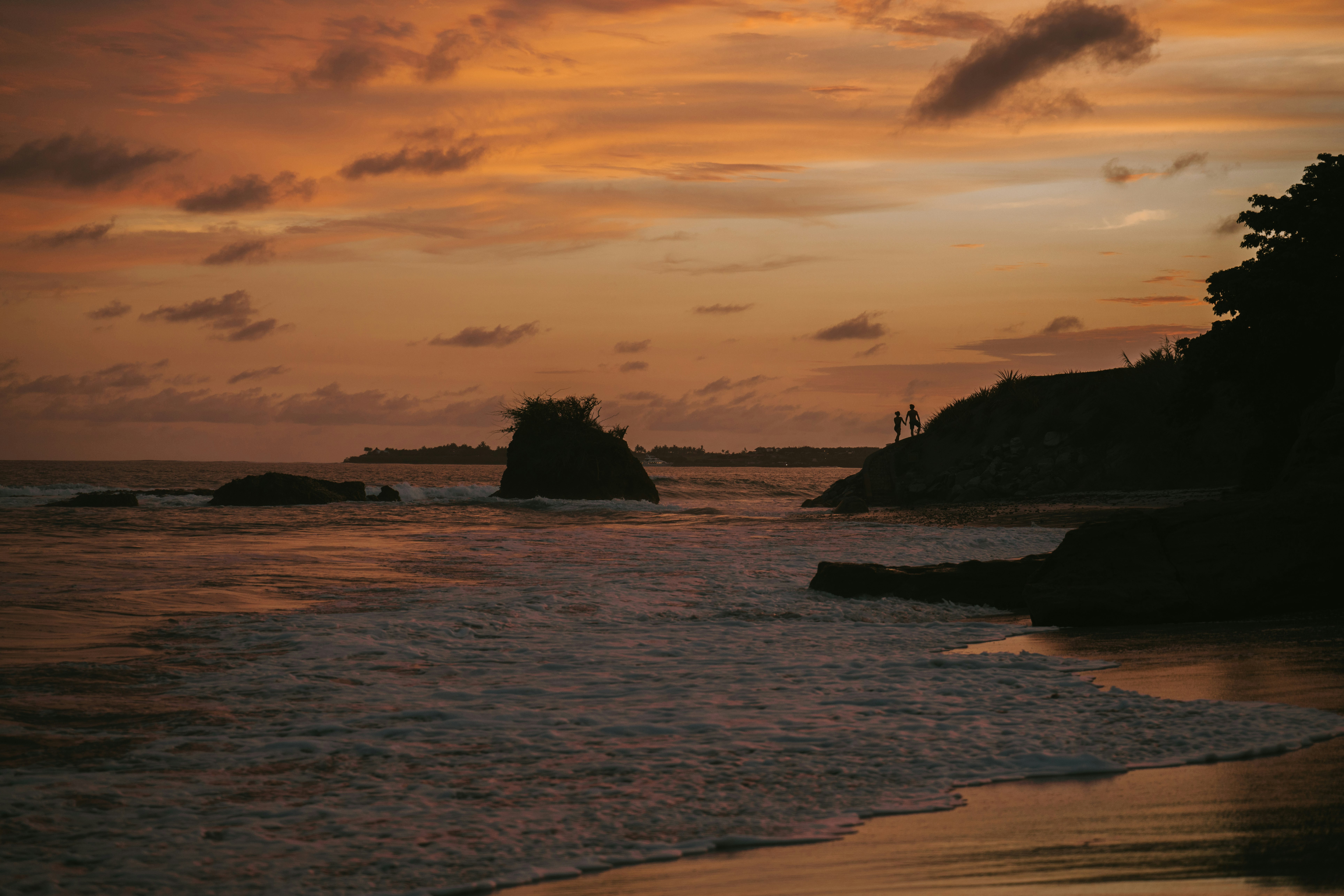 silhouette of rock formation on sea during sunset