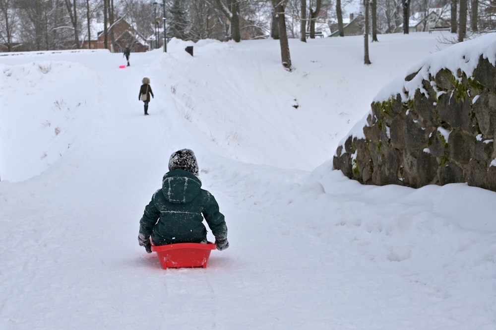 person in black jacket riding red sled on snow covered ground during daytime