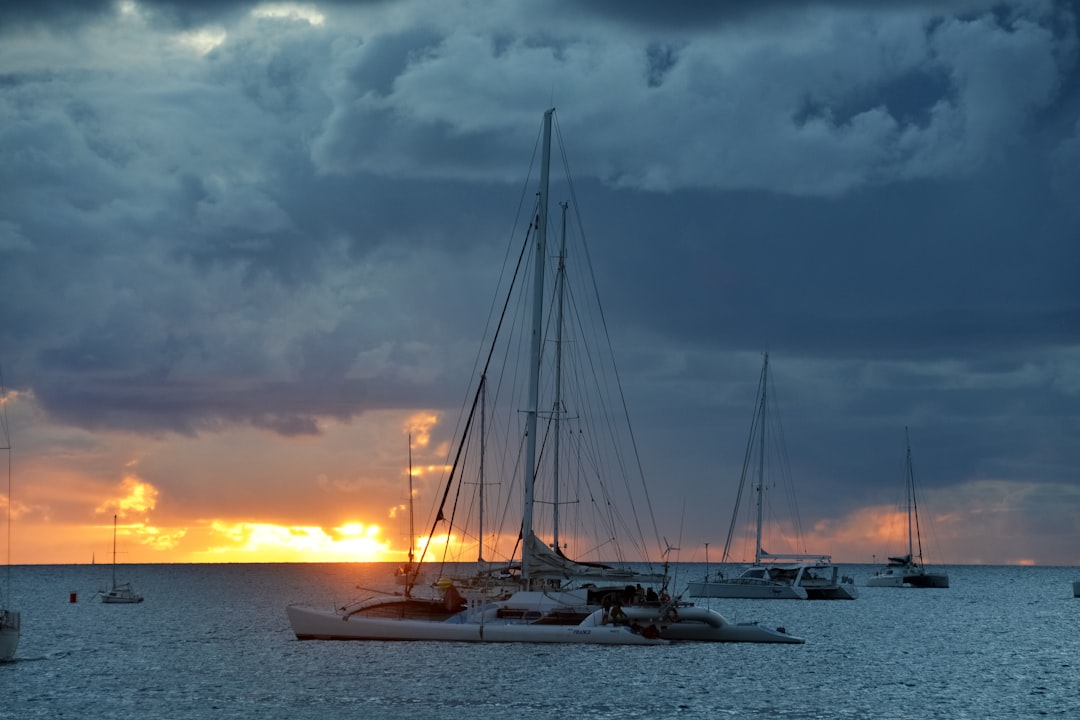 white sail boat on sea under cloudy sky during sunset