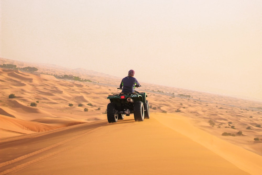 Uomo che guida un ATV nero sulla sabbia marrone durante il giorno