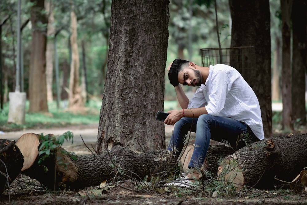 man in white dress shirt and blue denim jeans sitting on tree log during daytime