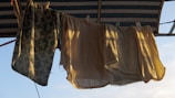 A line with clothespins holds several towels or cloths that hang in the warm sunlight. The pattern and texture of the towels are visible, with a floral design on one of them. The setting appears to be an outdoor area, possibly under a canopy or awning.