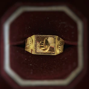 Elegant gold ring with intricate detailing displayed on a dark velvet cushion.