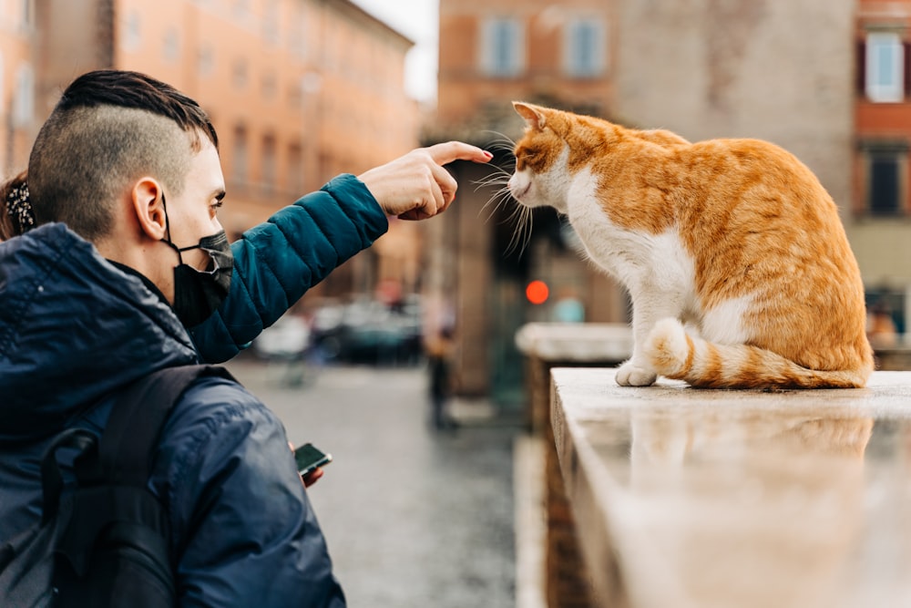 homem na jaqueta preta segurando o gato laranja e branco