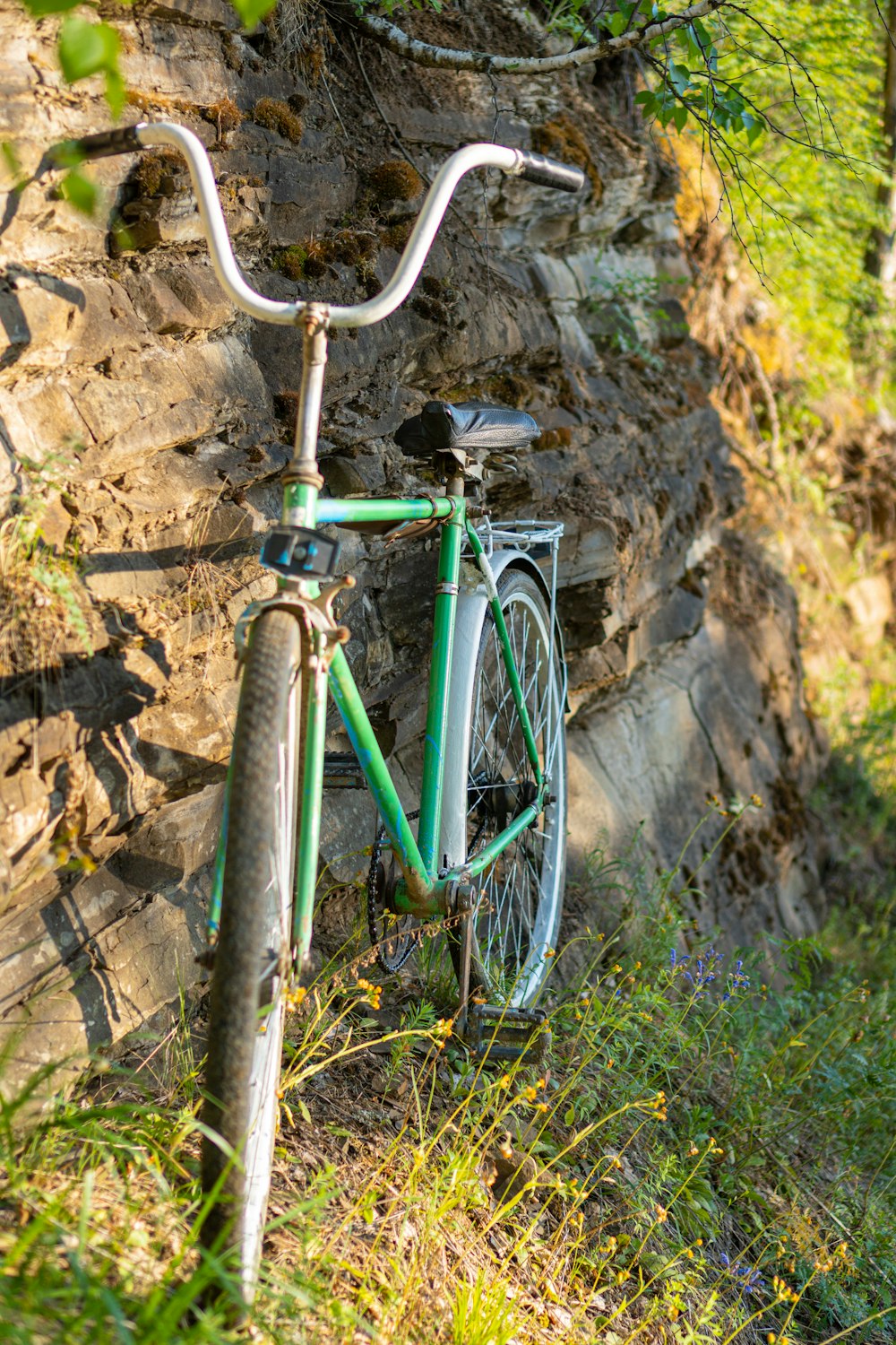 green bicycle leaning on brown rock wall
