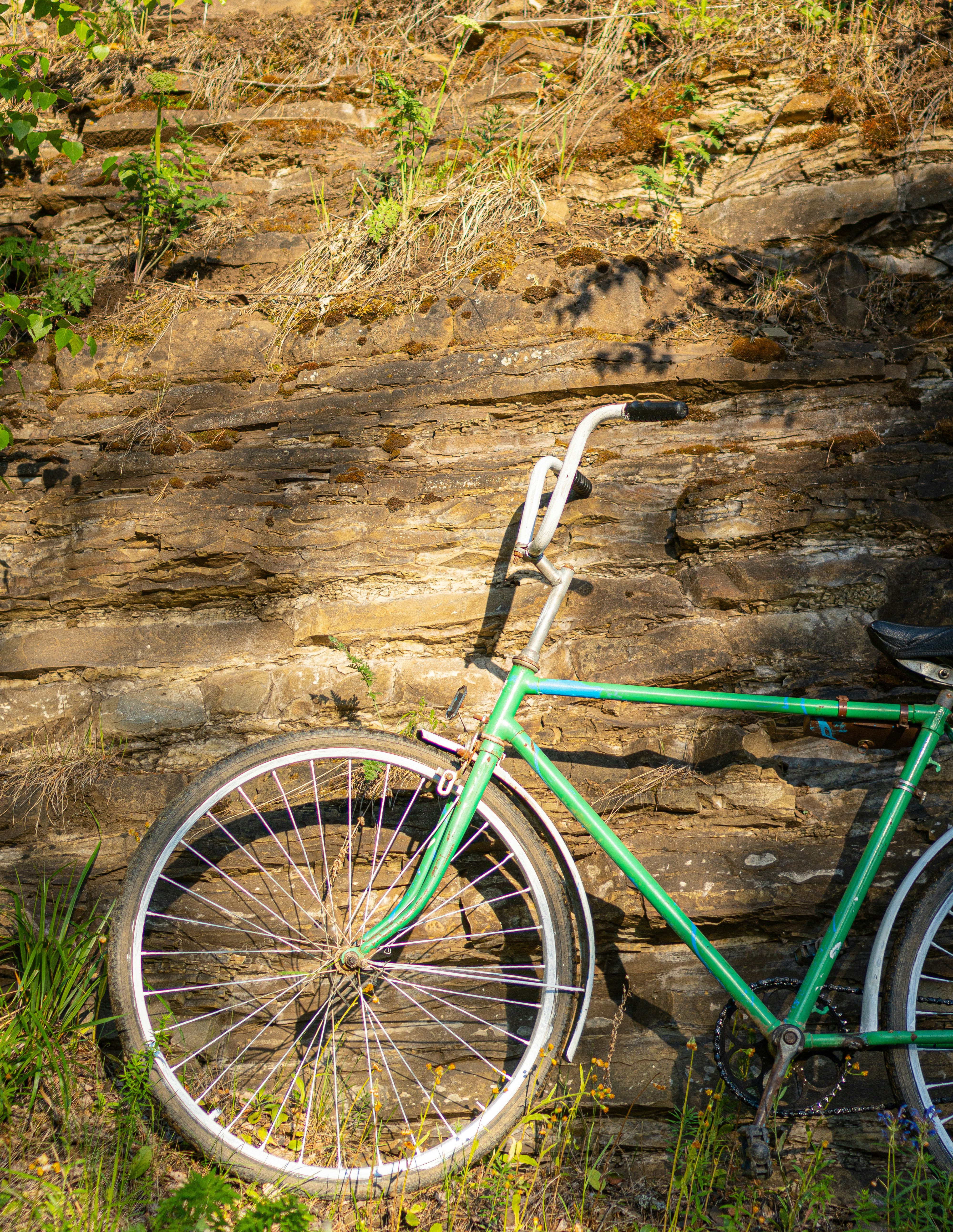 green bicycle leaning on brown rock wall