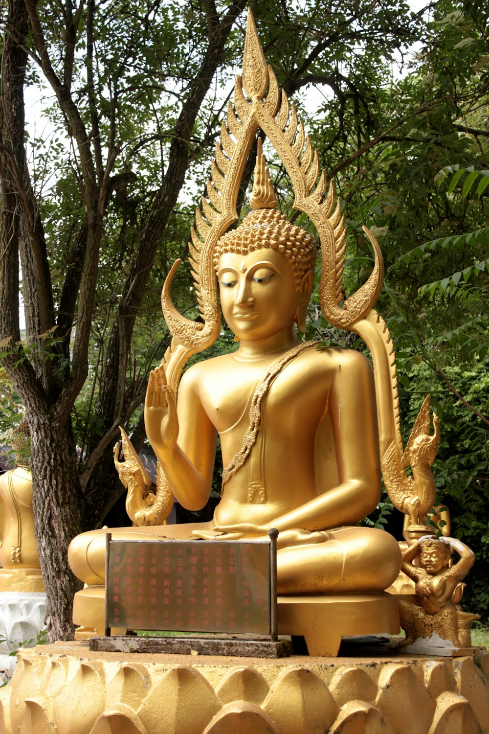 gold buddha statue near green trees during daytime