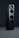 A sleek black audio speaker with a modern, minimalist design. The speaker consists of two stacked rectangular units, each featuring circular sound outputs. The top unit has a prominent cone-like speaker, while the bottom unit includes two additional circular drivers. The surface has a glossy finish, reflecting light subtly.